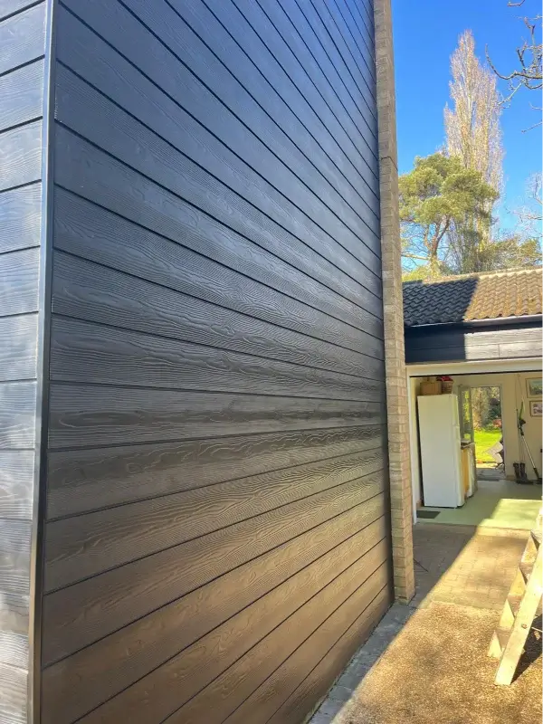 Close-up of dark grey woodgrain-effect horizontal cladding fitted to a two-storey exterior wall. By Norfolk Exterior Solutions.